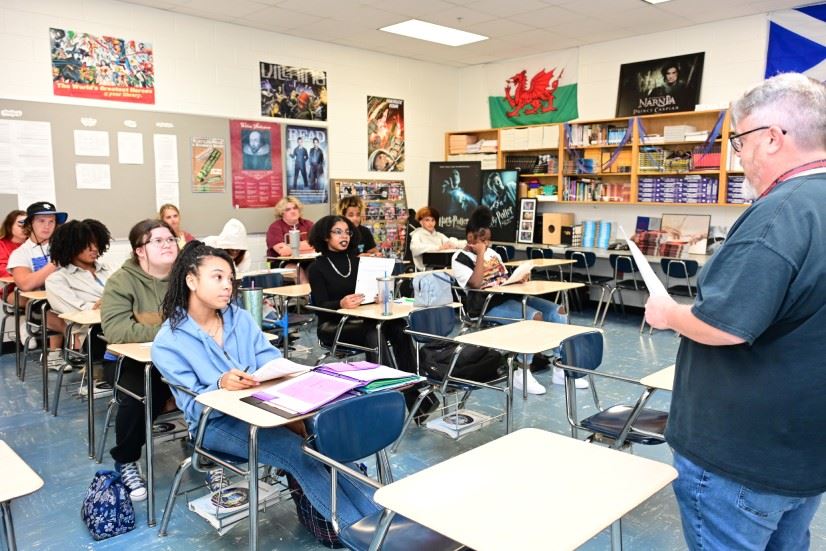  Male teacher facing class and engaging with seated high school students.